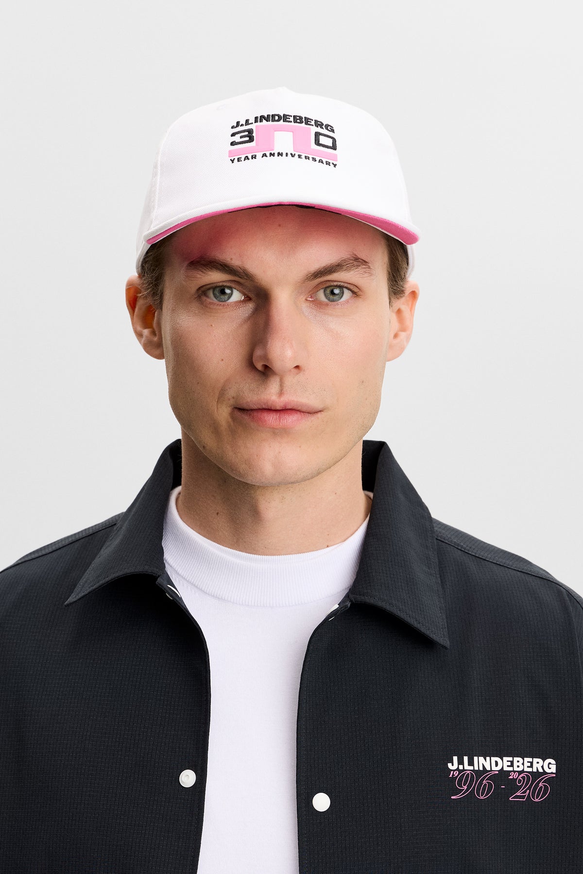 Gorra J.Lindeberg 30Y Anniversary Cap White: detalle de la marca del aniversario en la parte delantera y trasera